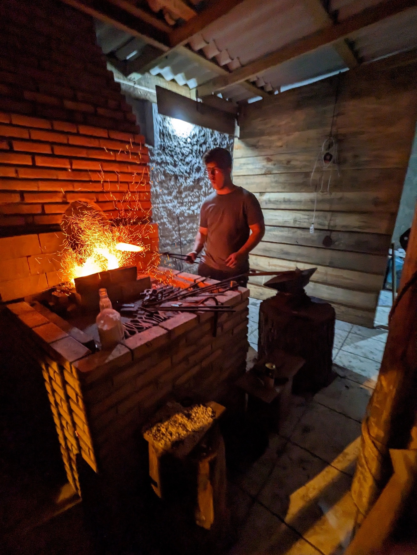 A blacksmith works beside a glowing charcoal forge